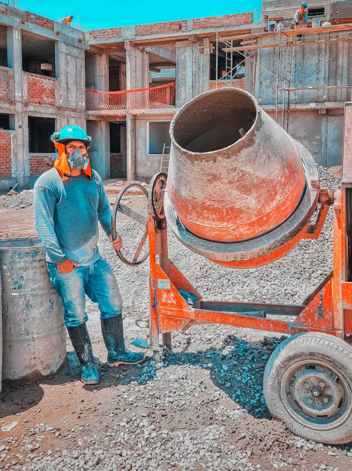 Home Construction worker operates heavy concrete mixer on sunny outdoor site.